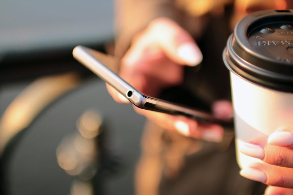 Person, die ein Smartphone und einen Kaffeebecher zum Mitnehmen hält, während sie im Freien eine SMS schreibt.
